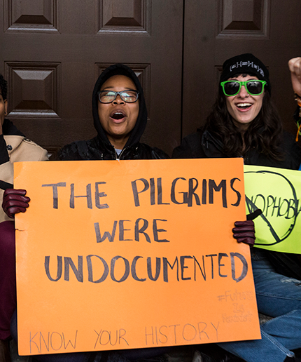 A protester holds a sign saying The Pilgrims were undocumented