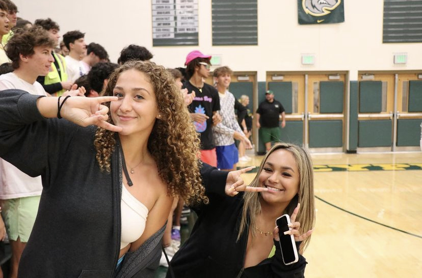 Juniors Kamila Angulo and Juliana Snyder throw up a bulls sign with a smile at an away volleyball game.